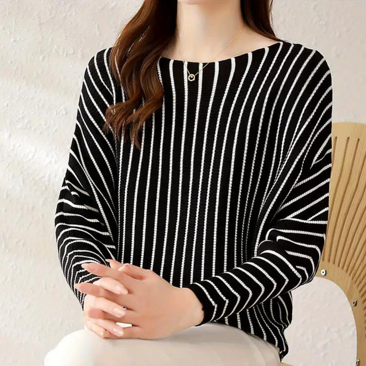 Vrouw in zwart-wit gestreepte trui, zittend op houten stoel. Modieuze dameskleding, casual stijl, comfortabele pasvorm.