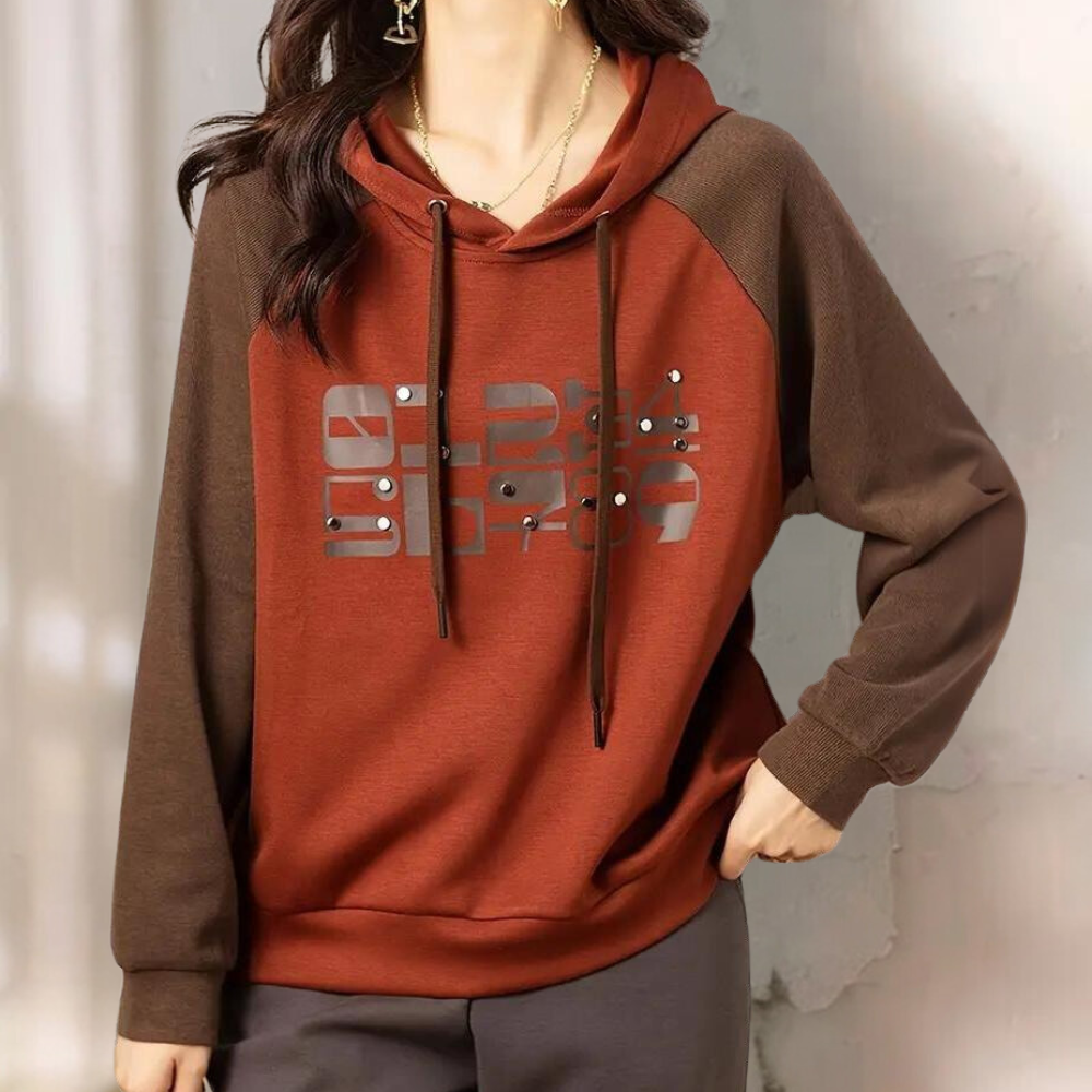 Vrouw draagt bruine en rode hoodie met grafische print, lange mouwen en capuchon. Modieuze dameskleding, casual stijl, comfortabele pasvorm.