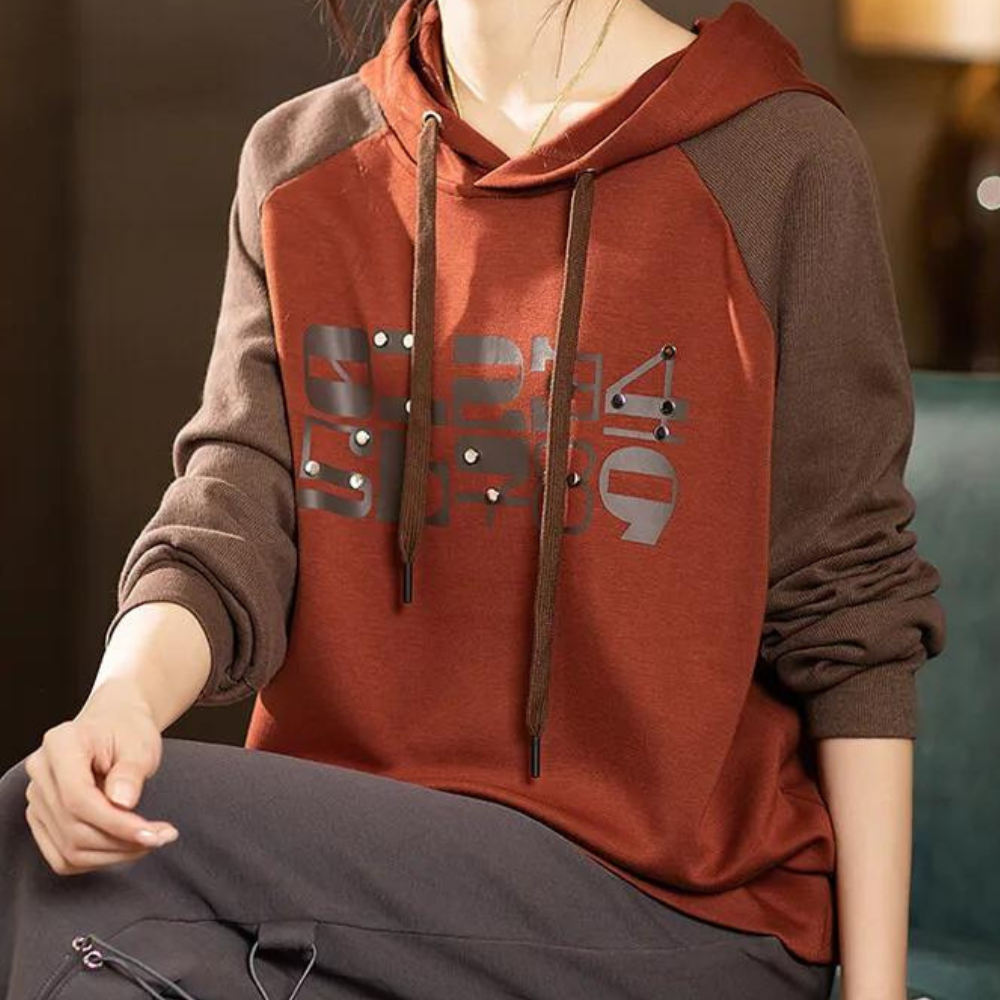 Vrouw draagt bruine en oranje hoodie met grafische print, comfortabele herfstmode, casual kleding voor dames, trendy streetwear stijl.
