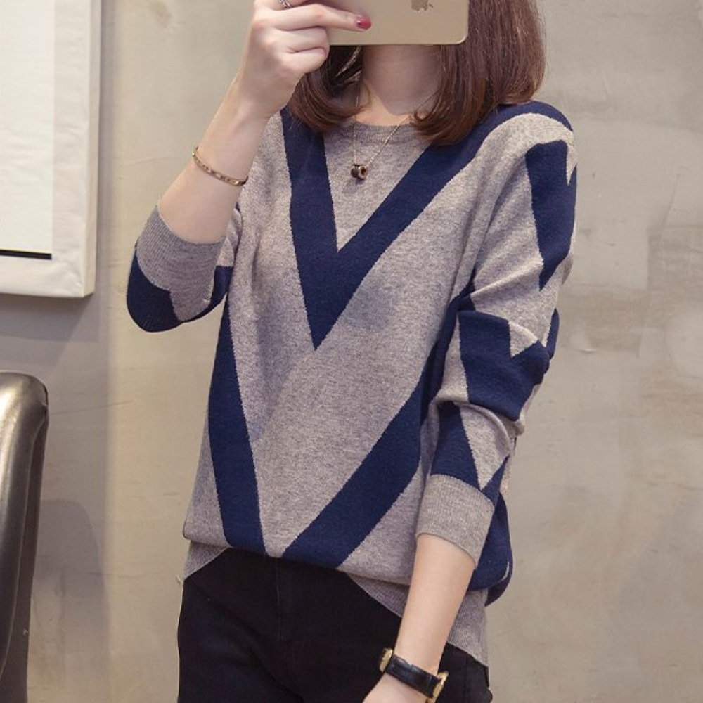 Grijze trui met blauwe geometrische V-patronen, gedragen door een vrouw. Modieuze dameskleding, herfst/winter stijl, casual chic outfit.