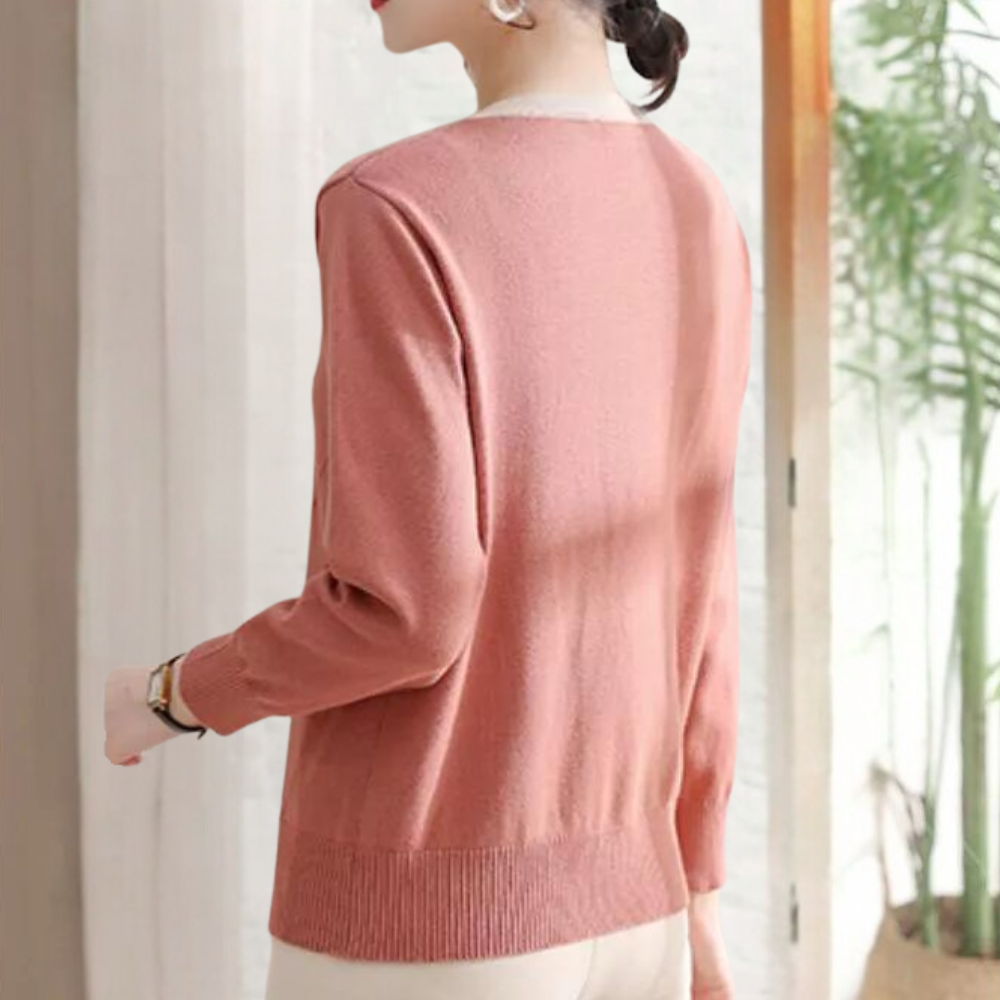 Vrouw in roze trui met lange mouwen, staand bij raam. Elegante damesmode, casual stijl, comfortabele kleding, herfstoutfit.