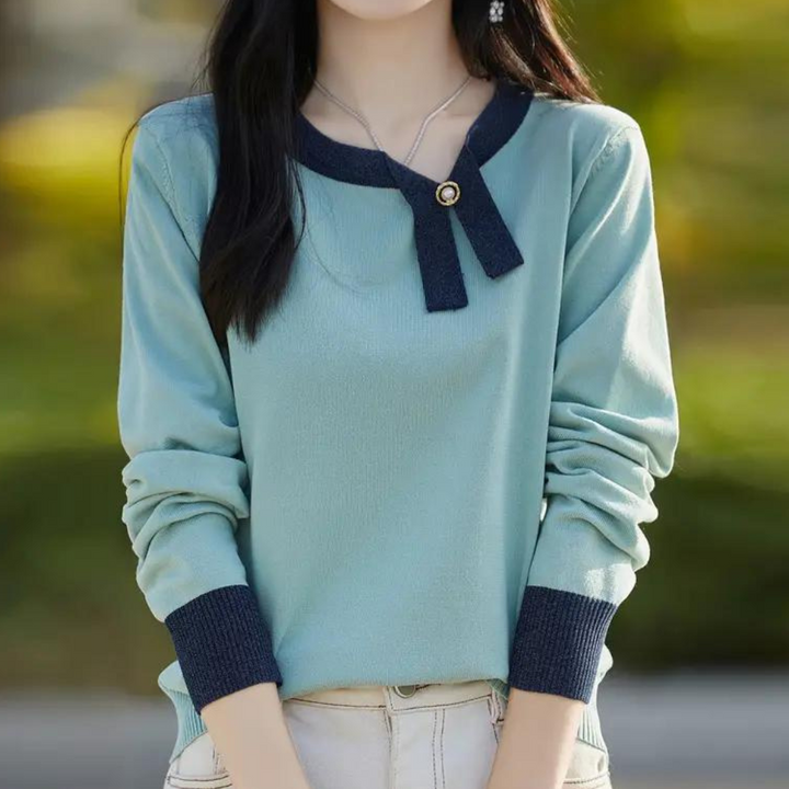 Vrouw in stijlvolle mintgroene trui met donkerblauwe accenten en knoopdetail, buiten gefotografeerd. Trendy damesmode, herfstkleding.
