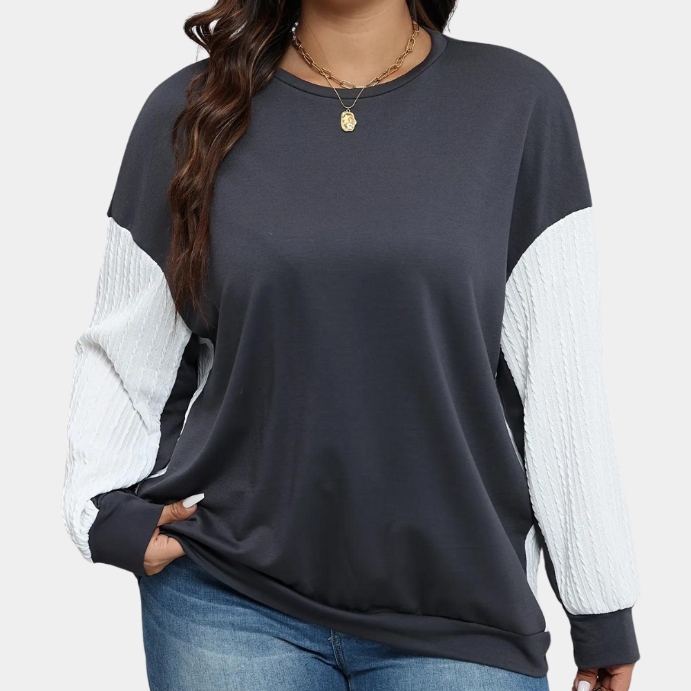 Vrouw draagt donkergrijze trui met witte mouwen, casual stijl, comfortabele pasvorm, ideaal voor herfstmode, gecombineerd met blauwe jeans.
