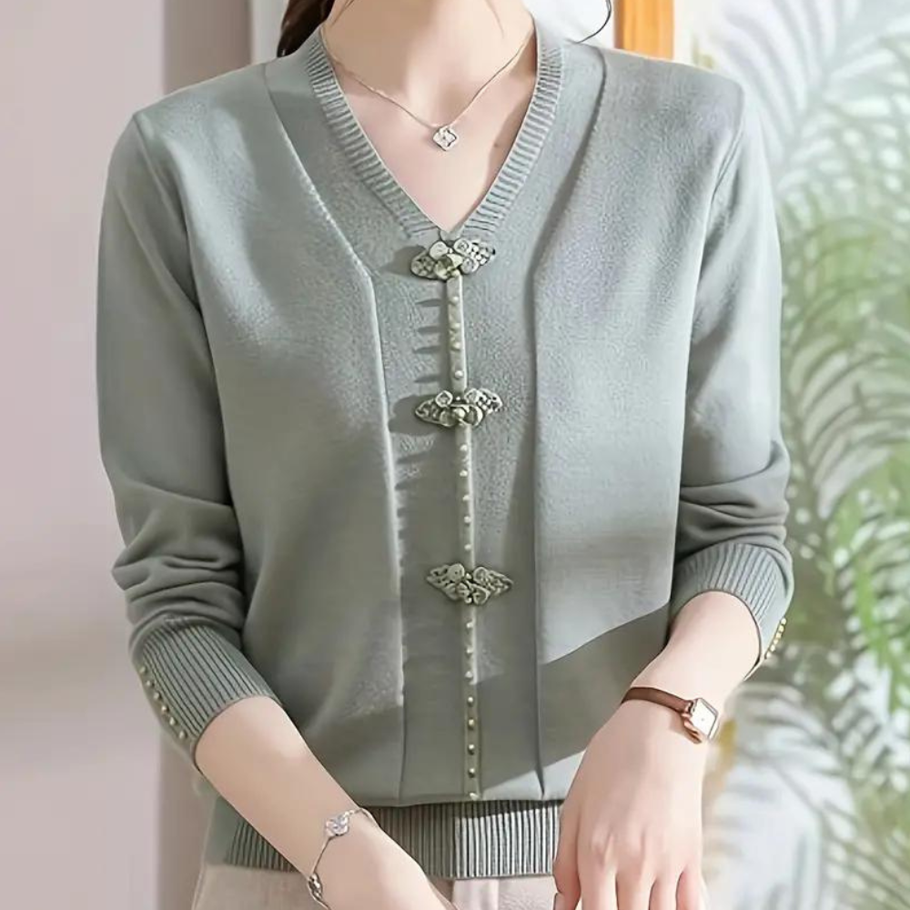 Vrouw draagt stijlvolle groene cardigan met V-hals en decoratieve knopen, gecombineerd met een zilveren ketting en horloge. Elegante damesmode.