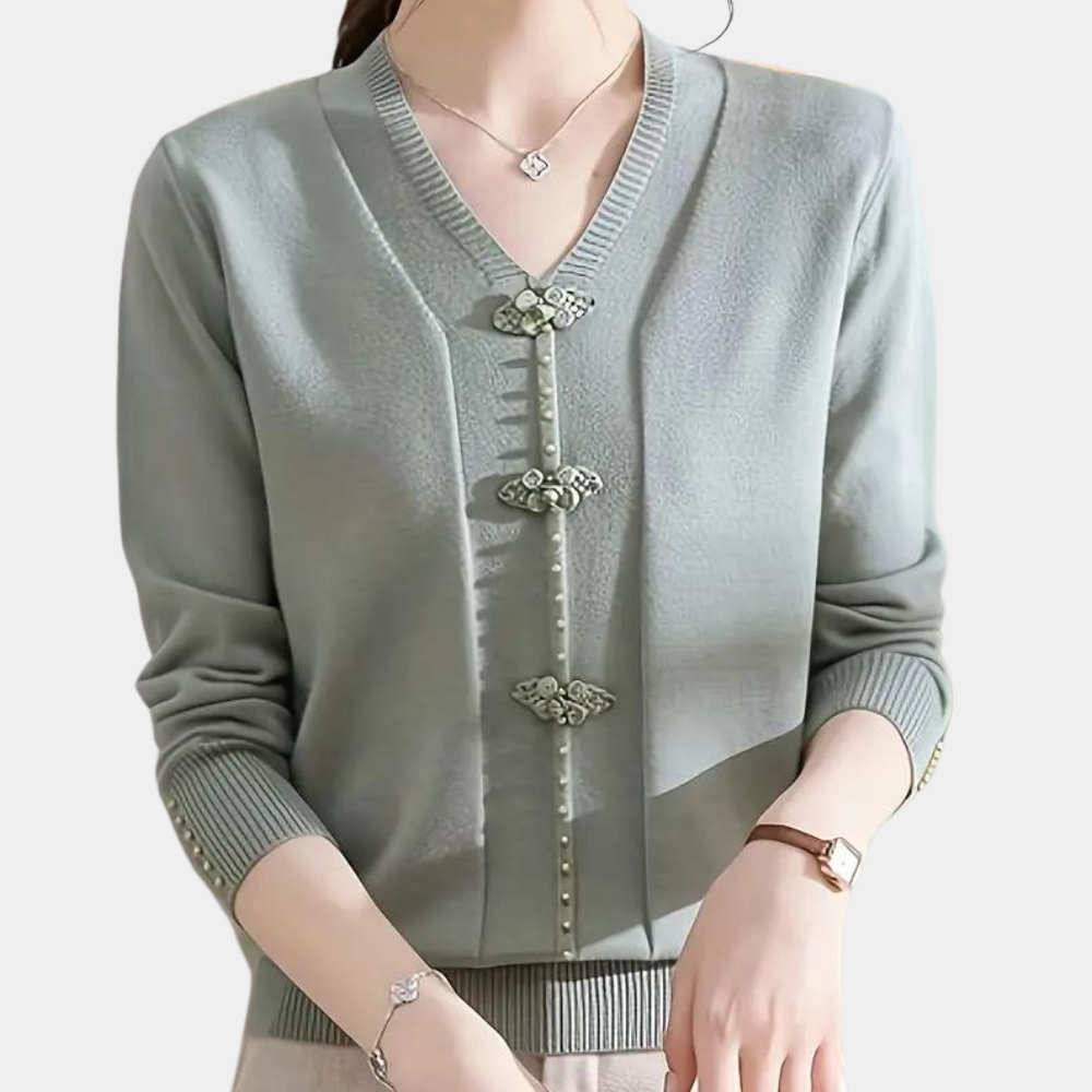 Vrouw draagt stijlvolle groene cardigan met V-hals en decoratieve knopen, gecombineerd met subtiele sieraden. Elegante damesmode, herfstkleding.