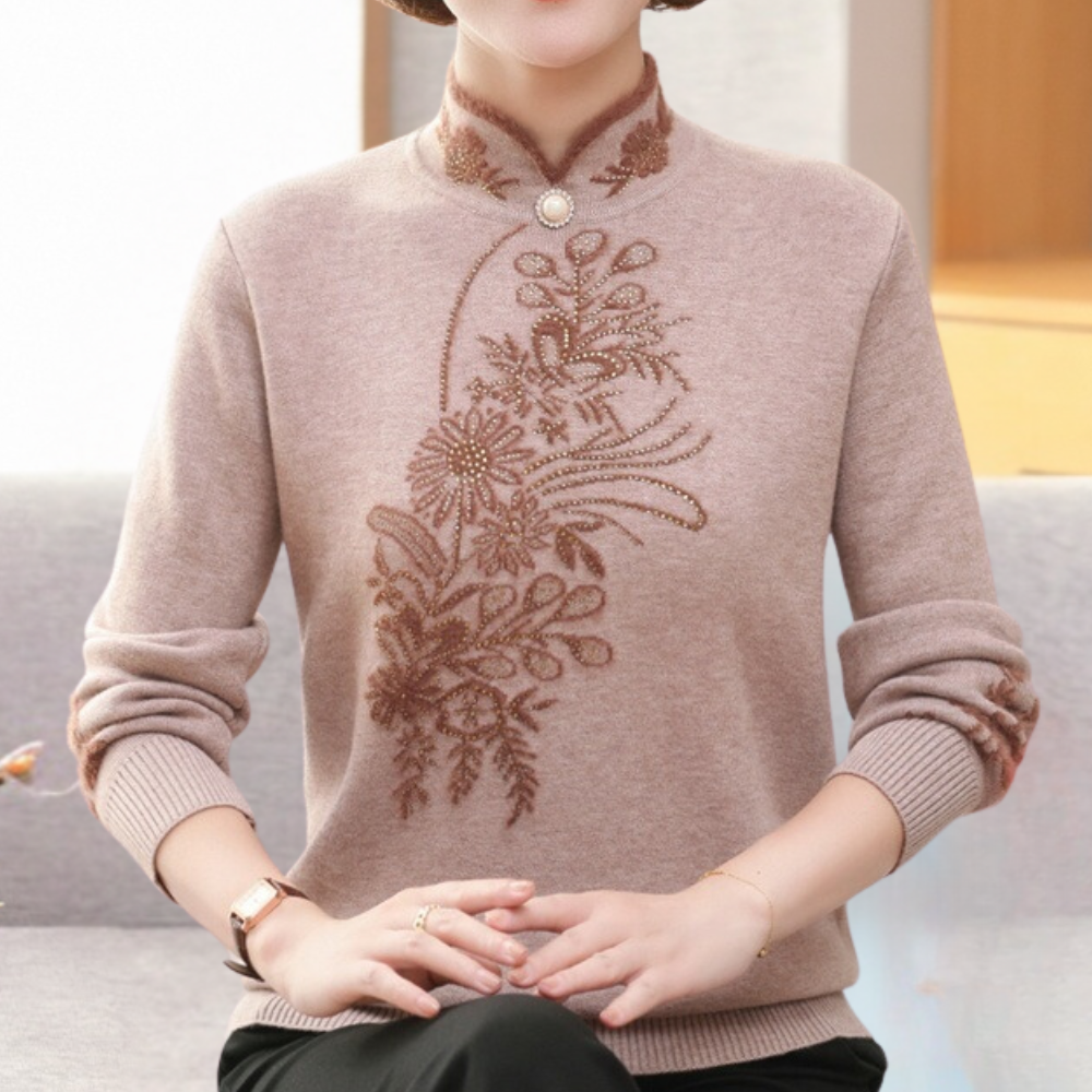 Vrouw draagt beige trui met bloemenborduursel, opstaande kraag en knoopdetail. Elegante damesmode, herfst-winter kleding, comfortabele pasvorm.