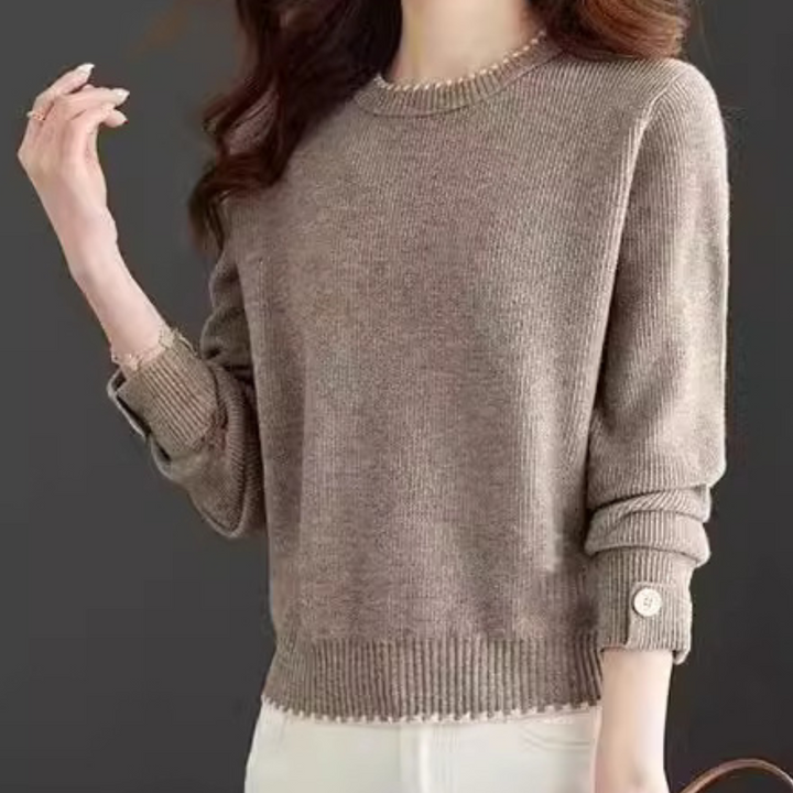 Vrouw draagt beige trui met lange mouwen en knoopdetails, gecombineerd met witte broek. Modieuze dameskleding, herfst/winter stijl.