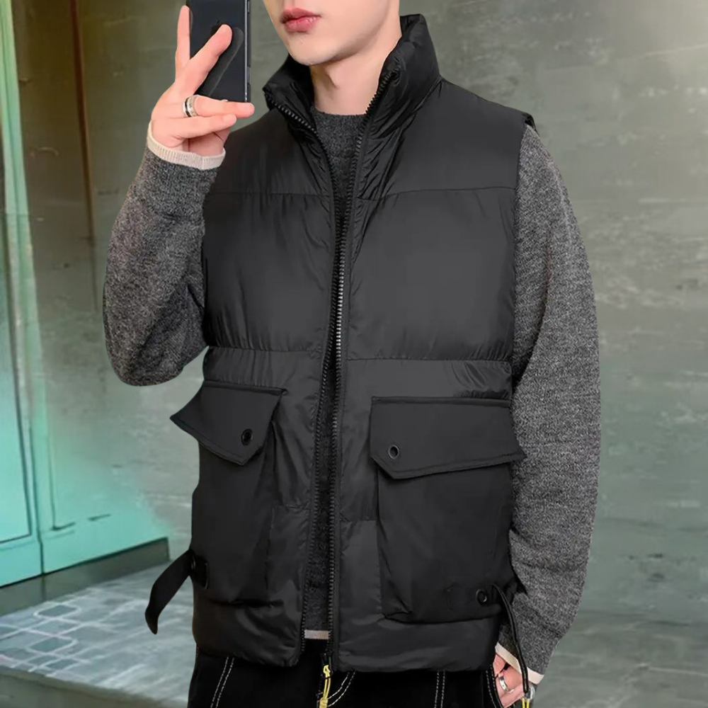 Jonge man in zwarte gewatteerde bodywarmer en grijze trui, houdt smartphone vast. Modieuze herenkleding, winteroutfit, casual stijl.