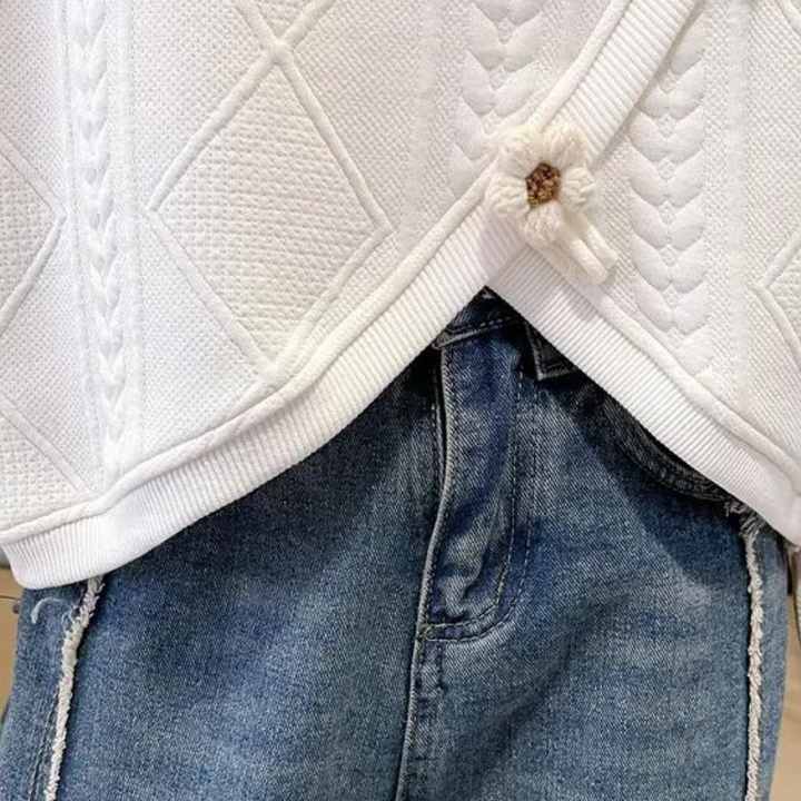 Witte gebreide trui met kabelpatroon en bloemdetail, gecombineerd met blauwe denim jeans. Modieuze dameskleding, herfst-winter stijl.