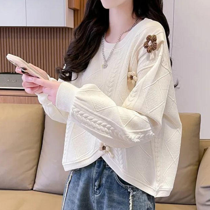 Vrouw in gebreide witte trui met bloemenpatroon, houdt smartphone vast. Modieuze casual outfit, ideaal voor herfst en winter.