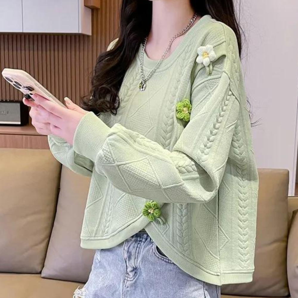 Vrouw in groene gebreide trui met bloemenpatroon, houdt smartphone vast. Trendy damesmode, casual outfit, comfortabele kledingstijl.