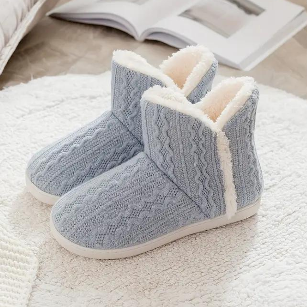 Lichtblauwe gebreide pantoffels met witte voering, warme winter sloffen, comfortabele dames huisschoenen op een witte vloermat.