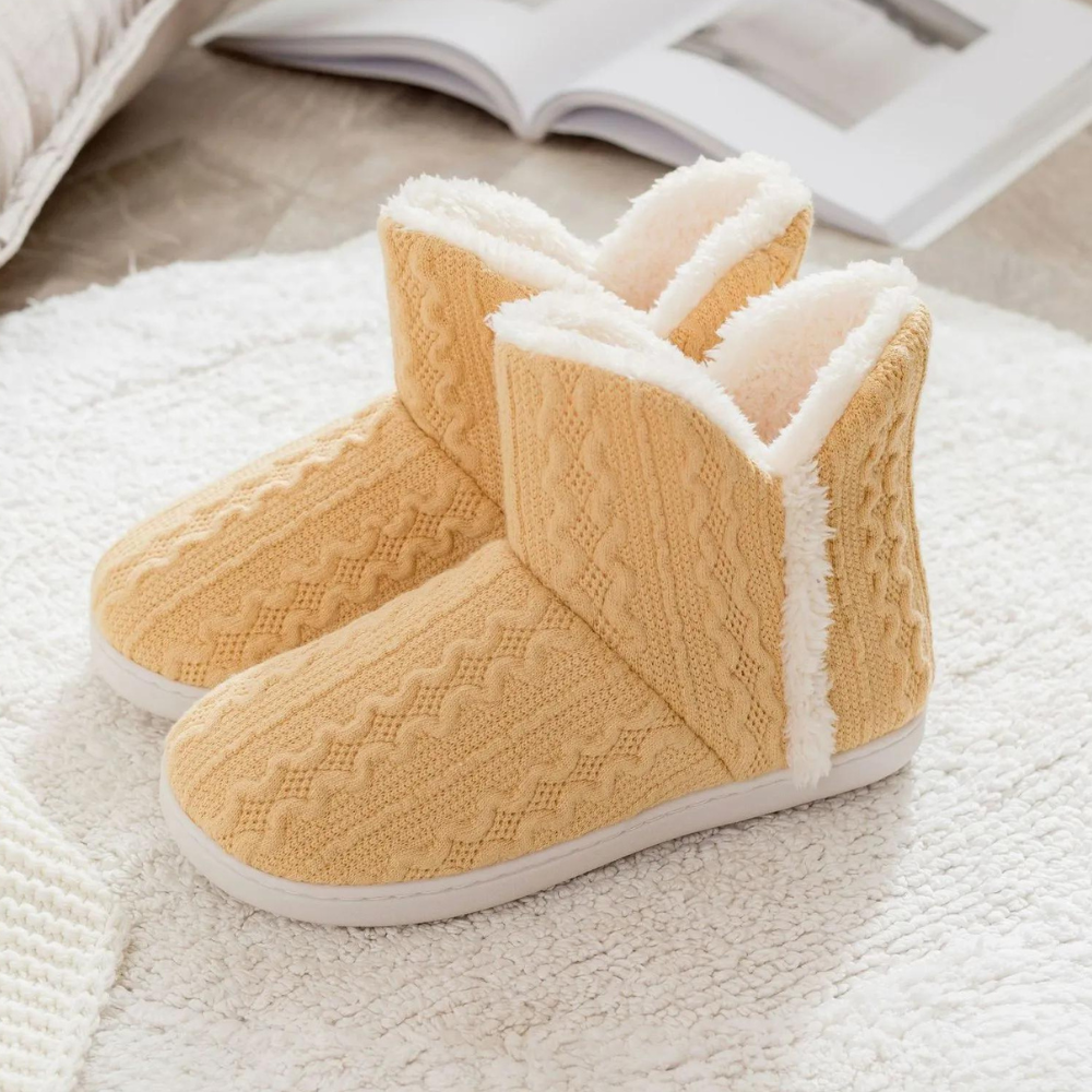 Gele gebreide pantoffels met witte voering op een zachte, witte ondergrond. Perfect voor wintercomfort en warme voeten.