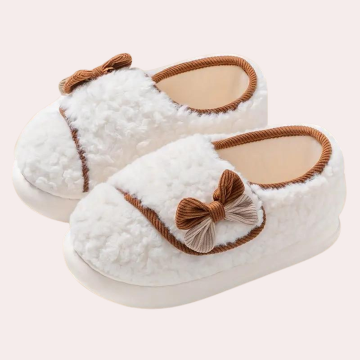Witte pluche babyslofjes met bruine strikjes, antislipzool en warme voering. Perfect voor comfort en stijl. Ideaal voor pasgeborenen.