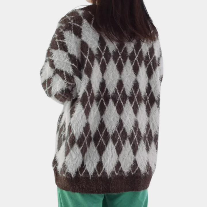 Vrouw draagt oversized trui met bruin-wit ruitpatroon, gecombineerd met groene broek. Modieuze winterkleding, comfortabele stijl.