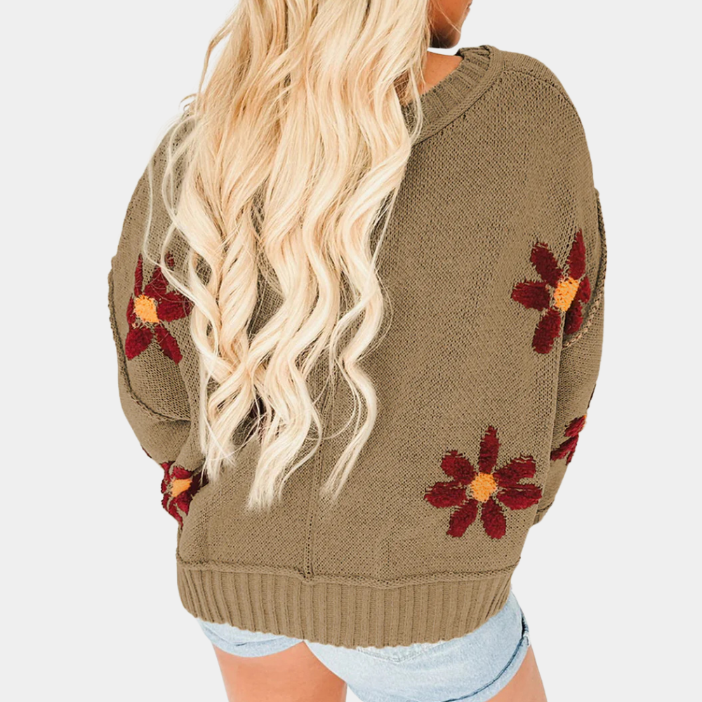 Vrouw in olijfgroene trui met rode bloemenprint, lange blonde haren, draagt denim shorts. Trendy herfstmode, casual dameskleding.