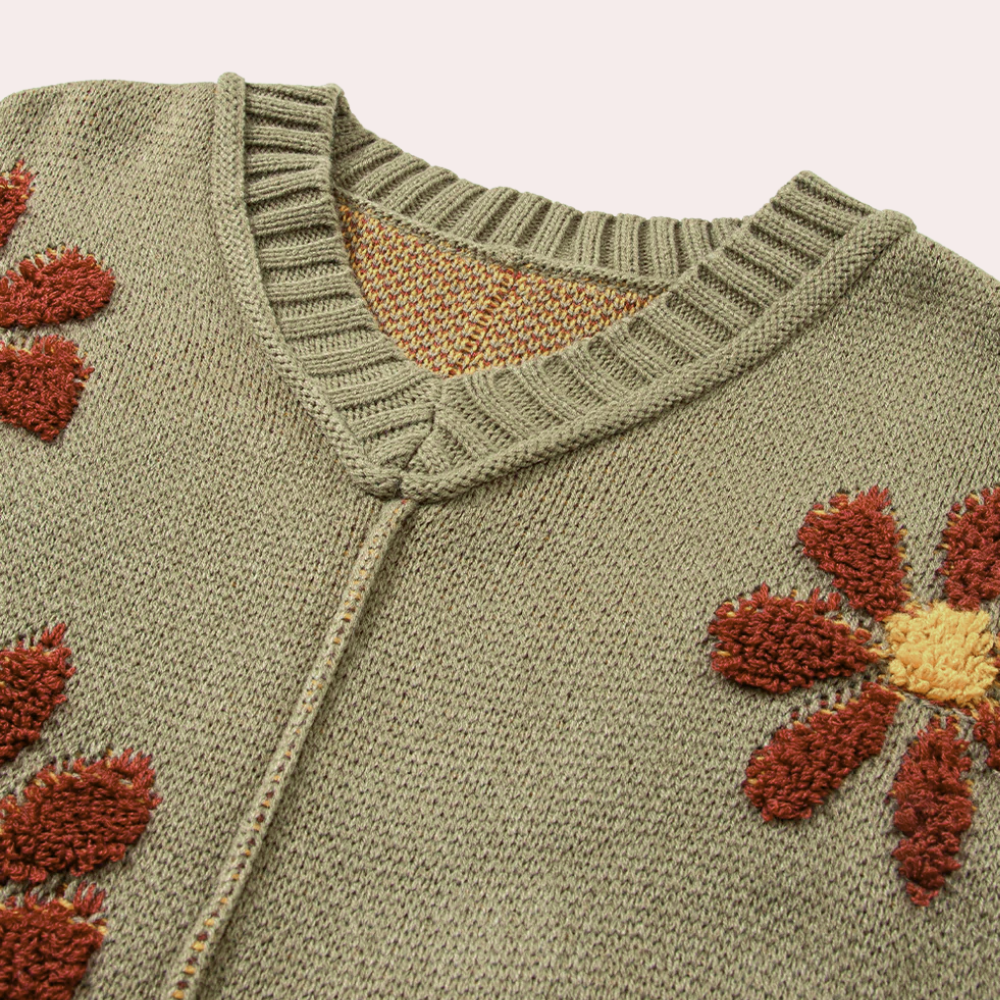 Groene gebreide trui met V-hals, versierd met rode en gele bloemenpatronen. Perfect voor herfstmode en casual outfits.