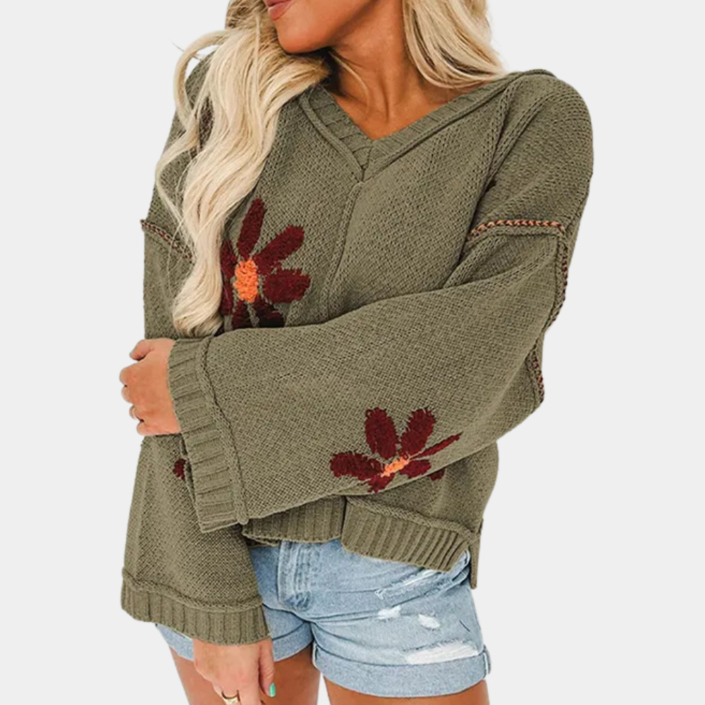 Vrouw in olijfgroene trui met bloemenpatroon en wijde mouwen, gecombineerd met denim shorts. Trendy herfstmode, casual dameskleding.