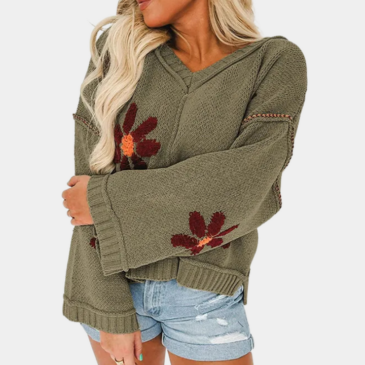 Vrouw in olijfgroene trui met bloemenpatroon en wijde mouwen, gecombineerd met denim shorts. Trendy herfstmode, casual dameskleding.