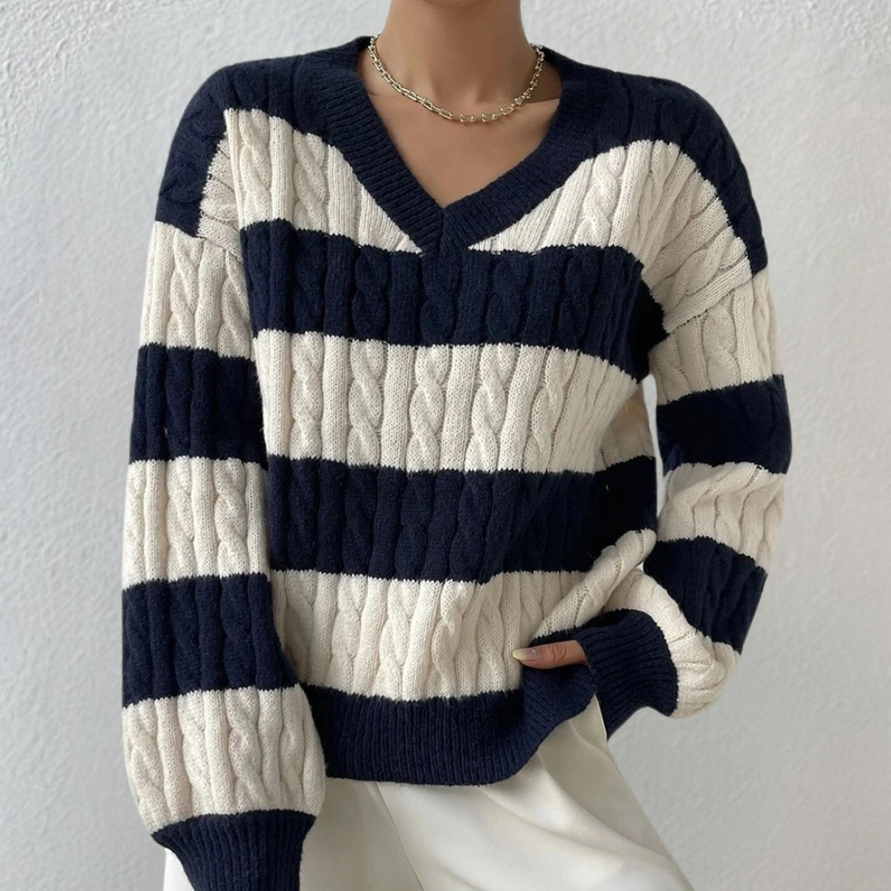 Donkerblauwe en witte gestreepte kabeltrui met V-hals, gedragen door een model. Stijlvolle damesmode, perfect voor herfst- en winterseizoenen.