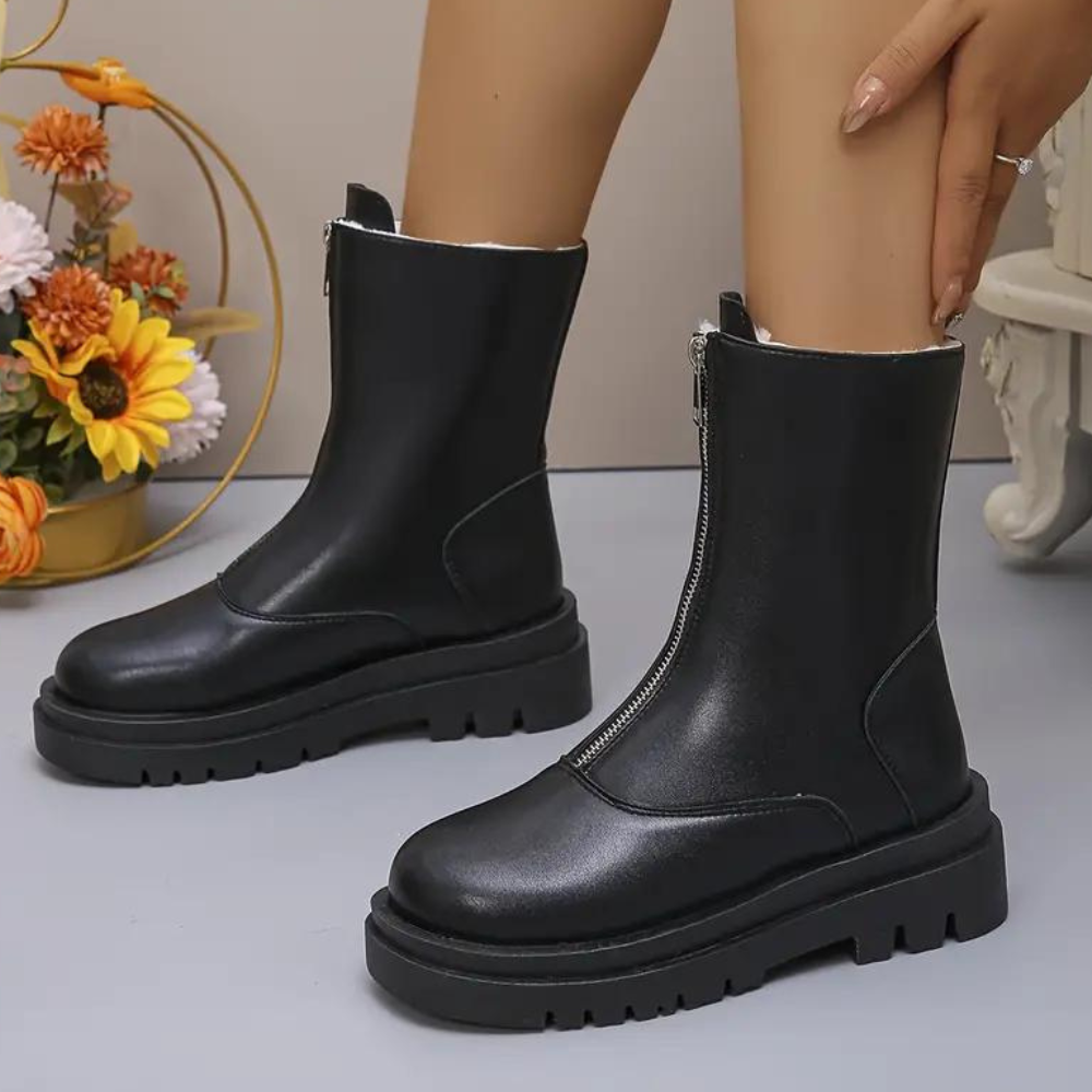Zwarte leren enkellaarsjes met ritssluiting, dikke zool en bloemen op de achtergrond. Trendy damesmode, comfortabele herfst- en winterlaarzen.