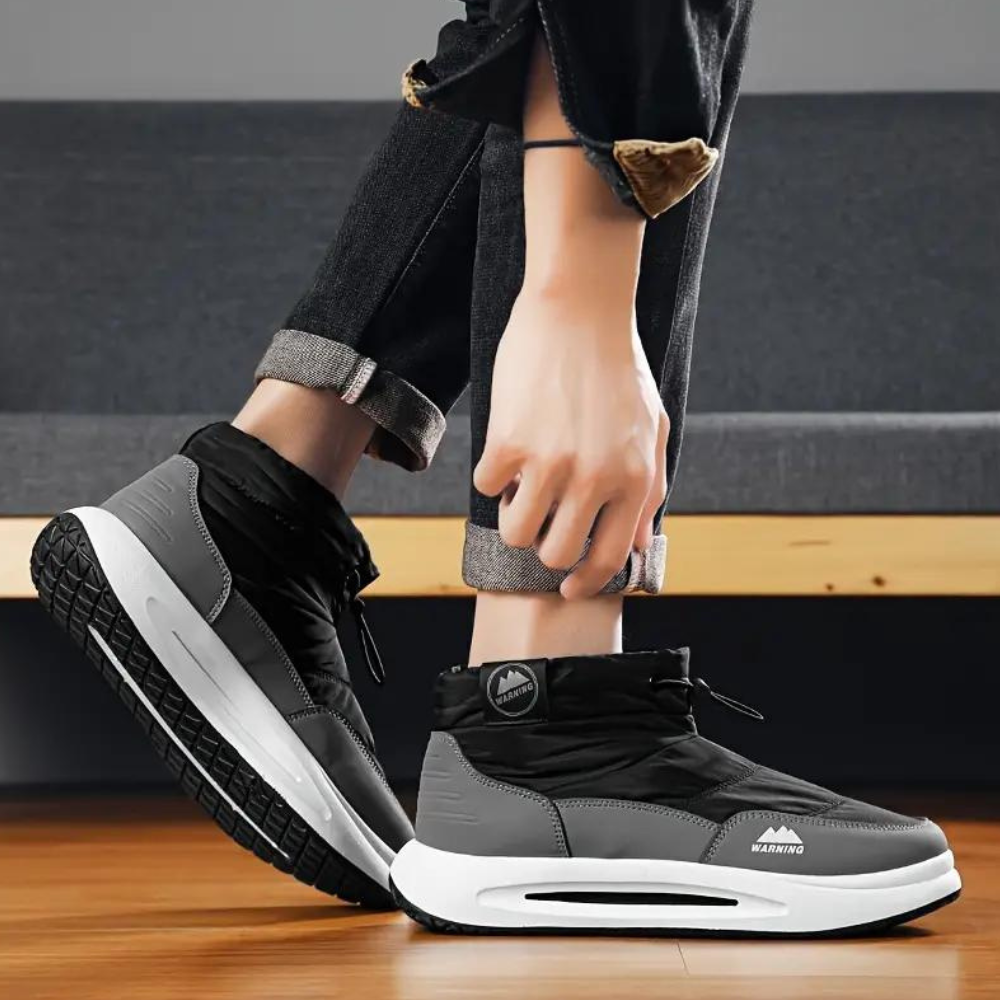 Grijze hoge sneakers met zwarte zool en witte accenten, gedragen door persoon op houten vloer. Moderne sportschoenen, casual stijl, unisex design.