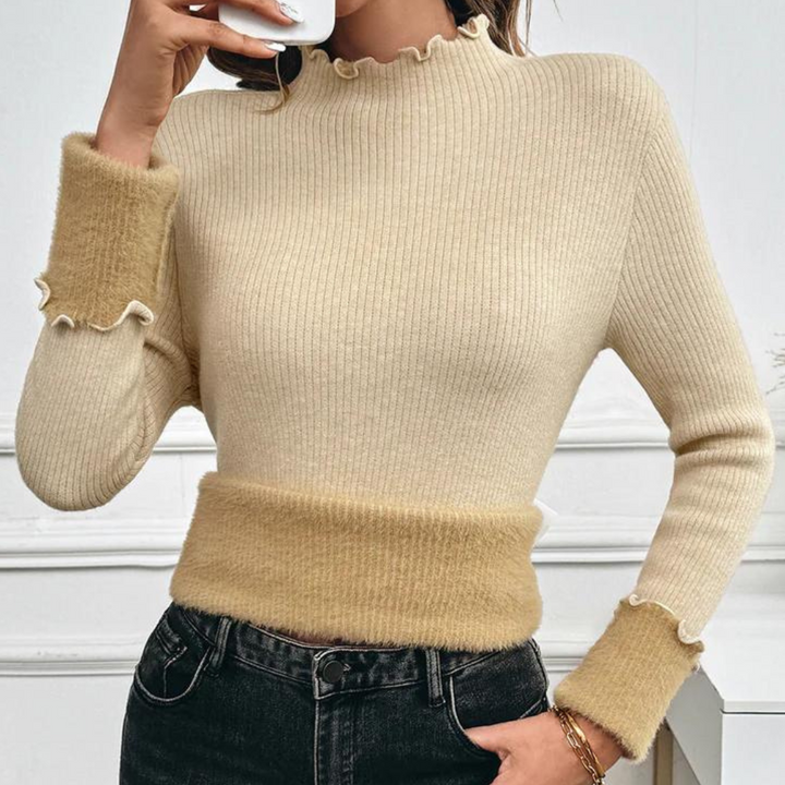 Vrouw draagt beige geribbelde trui met ruches, gecombineerd met zwarte jeans. Modieuze dameskleding, herfststijl, casual outfit.