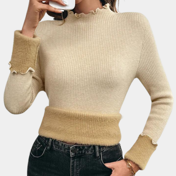 Vrouw draagt beige geribbelde trui met opstaande kraag en contrasterende manchetten, gecombineerd met zwarte jeans. Modieuze dameskleding.