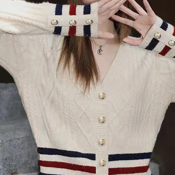 Beige kabeltrui met gouden knopen, rode en blauwe strepen op mouwen en taille, modieuze dameskleding, herfst-winter stijl.