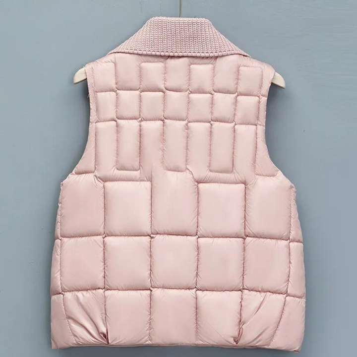Roze gewatteerd dames bodywarmer, mouwloos, met vierkant patroon, opgehangen aan een houten hanger tegen een blauwe achtergrond.