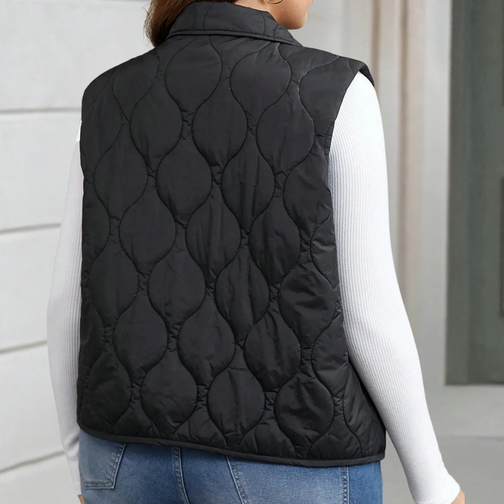 Zwarte gewatteerde bodywarmer voor dames, gedragen over een witte trui. Stijlvolle en warme kleding, ideaal voor herfst- en wintermode.