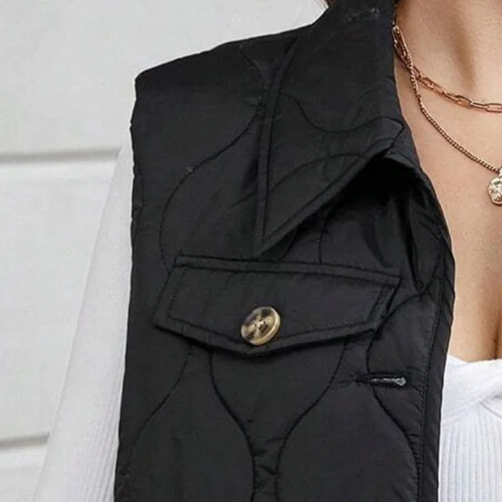 Zwarte gewatteerde bodywarmer met knoopsluiting, gedragen over een witte trui. Modieuze dameskleding, herfst- en winterstijl.