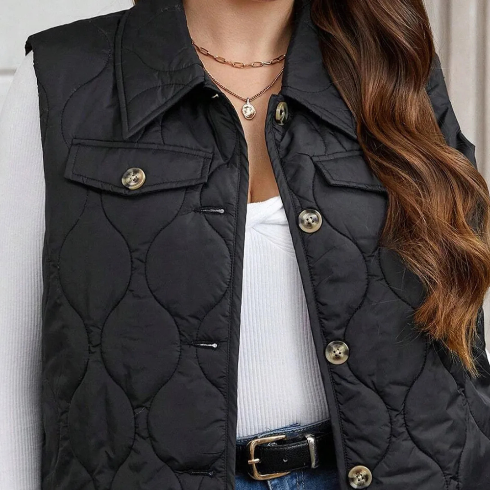 Dames zwarte gewatteerde bodywarmer met knopen, gedragen over witte trui. Modieuze herfstkleding, casual stijl, geschikt voor dagelijks gebruik.