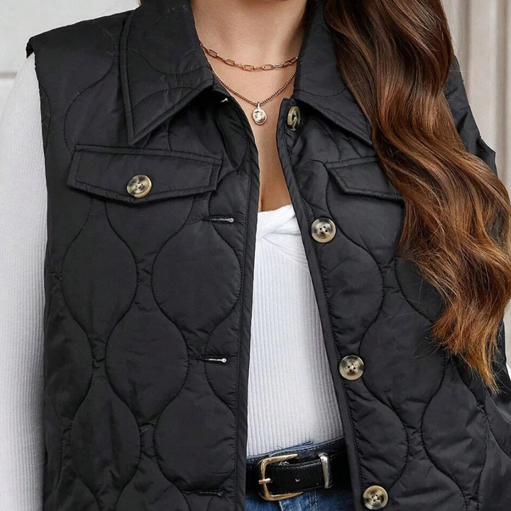 Dames zwarte gewatteerde bodywarmer met knopen, gedragen over witte trui. Modieuze herfstkleding, casual stijl, geschikt voor dagelijks gebruik.