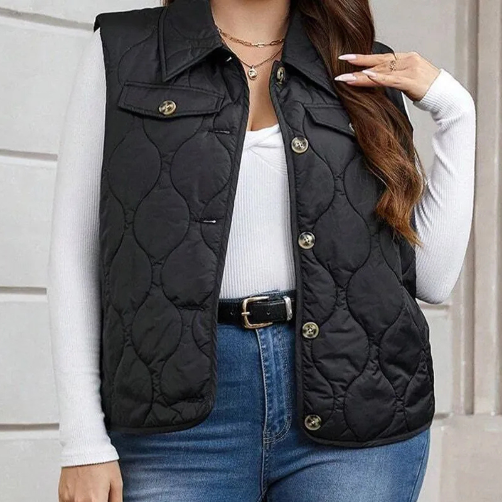 Dames zwarte gewatteerde bodywarmer, knoopsluiting, gedragen over witte top en jeans. Modieuze herfstkleding, casual stijl.