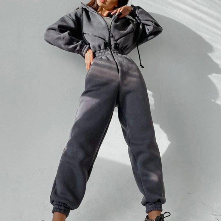 Grijze dames jumpsuit met capuchon, lange mouwen en elastische taille. Modieuze streetwear outfit voor casual en comfortabele stijl.