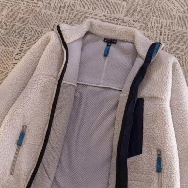 Witte fleece jas met ritsen en blauwe accenten, liggend op krantenpapier. Warme winterjas, modieus en comfortabel, ideaal voor koude dagen.