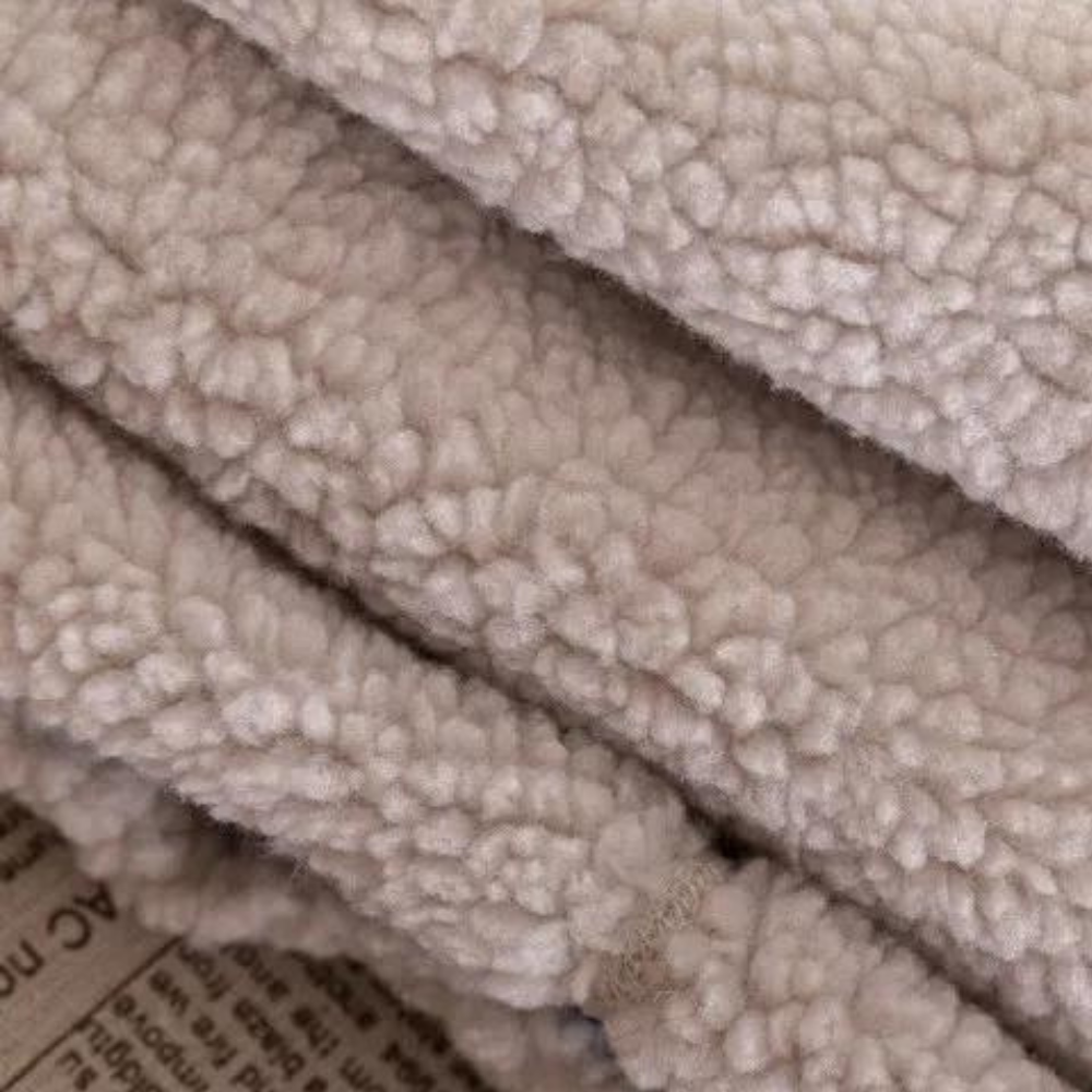 Zachte beige sherpa fleece stof, close-up textuur. Ideaal voor warme kleding en dekens. Populair in wintermode en interieurdecoratie.