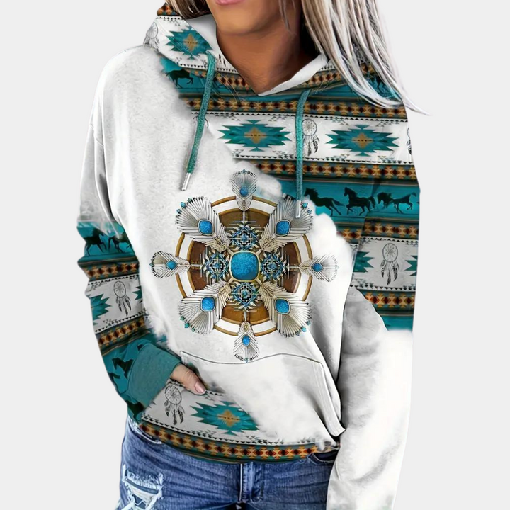 Vrouw draagt witte hoodie met turquoise en bruine Azteekse print, centrale mandala met schelpen en turquoise steen, casual mode, bohemian stijl.