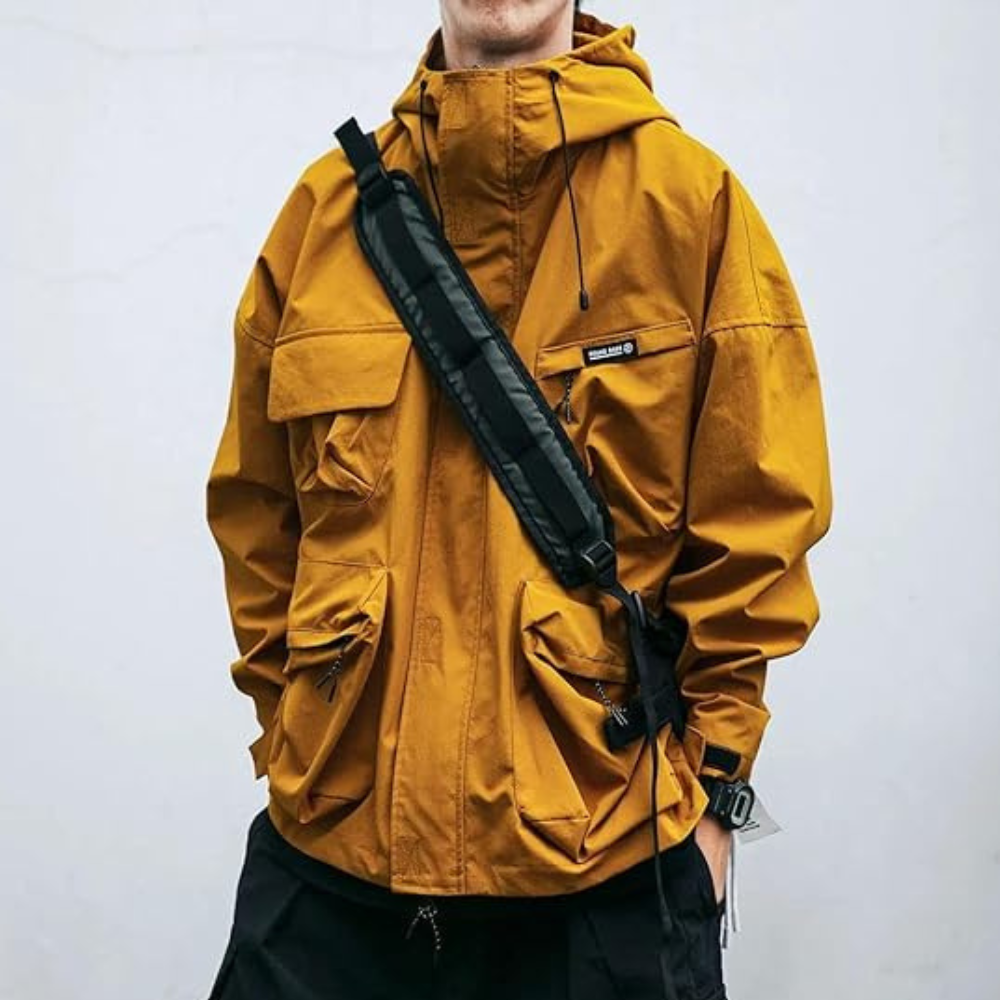 Man in gele waterdichte jas met capuchon en meerdere zakken, draagt een zwarte schoudertas. Stijlvolle outdoor kleding voor heren.