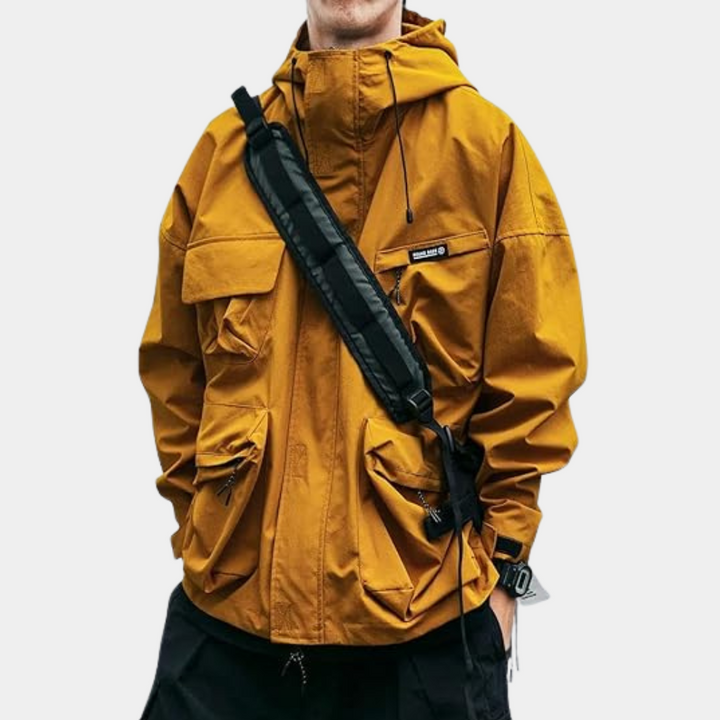 Gele herenjas met capuchon, meerdere zakken en zwarte schoudertas. Stijlvolle streetwear, ideaal voor herfstmode.