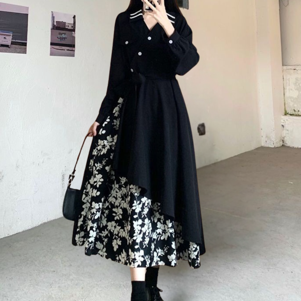 Zwarte asymmetrische jurk met bloemenprint, lange mouwen en dubbele knopen, gecombineerd met zwarte enkellaarsjes en een handtas.