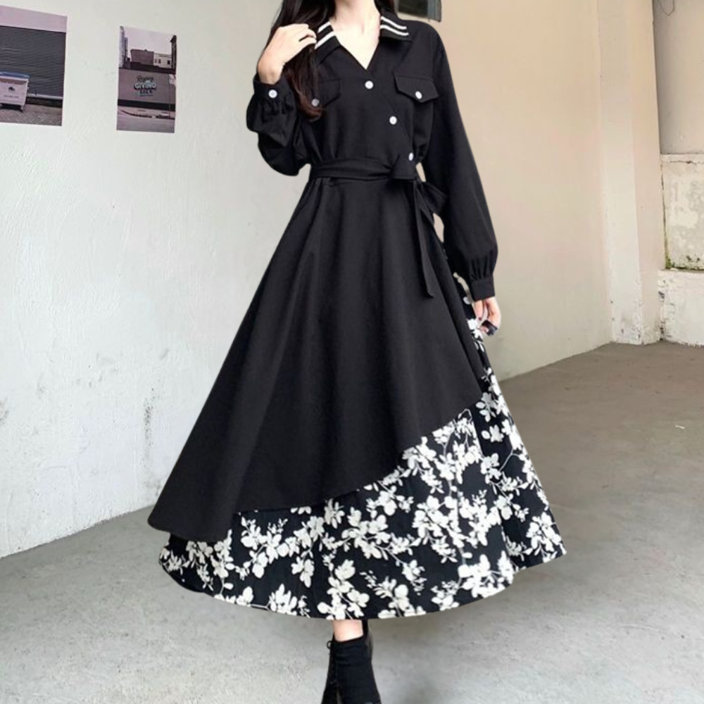 Zwarte lange jurk met bloemenprint, knoopsluiting en ceintuur, gedragen door vrouw in minimalistische ruimte. Elegante damesmode, herfstcollectie.