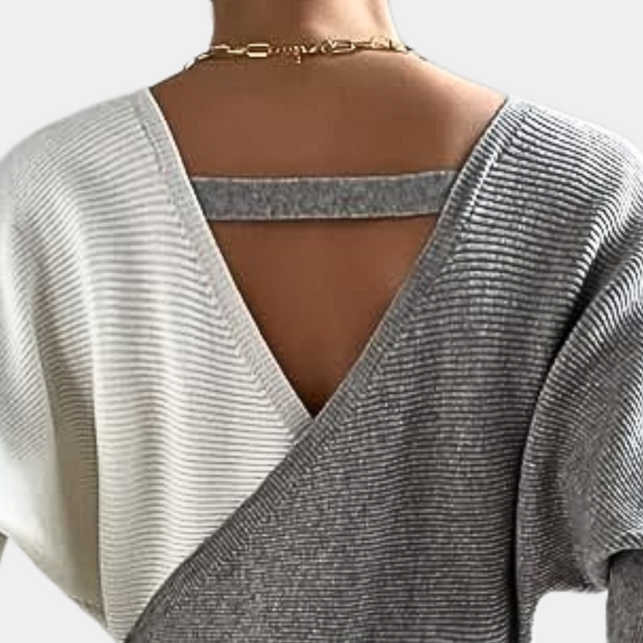 Grijze en witte gebreide trui met V-hals en open rug, gedragen door een model. Modieuze dameskleding, herfst-winter stijl, comfortabele pasvorm.