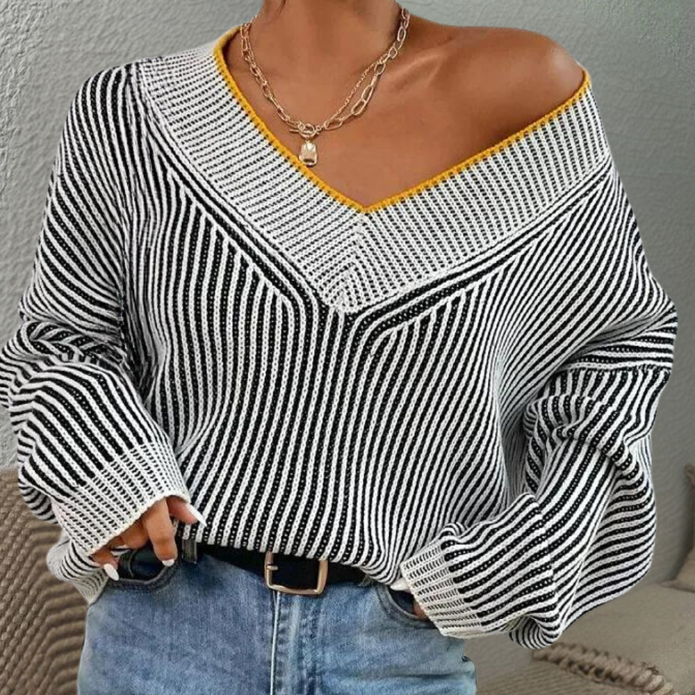 Vrouw draagt gestreepte trui met V-hals en gele rand, gecombineerd met blauwe jeans en ketting. Modieuze dameskleding, casual stijl.