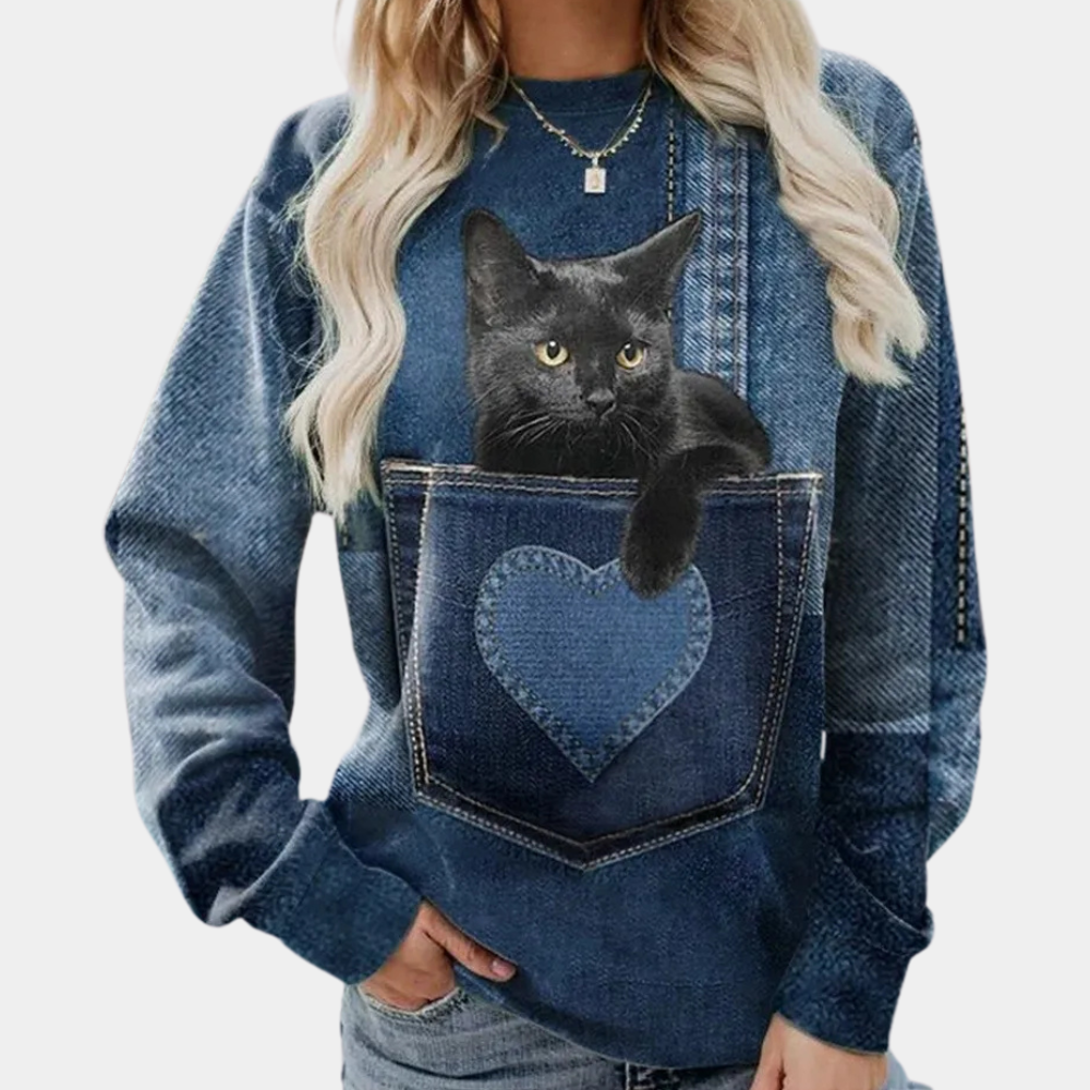 Vrouw draagt denim-look trui met zwarte kat in hartvormige zak. Modieuze dameskleding, casual stijl, dierenprint, trendy outfit.