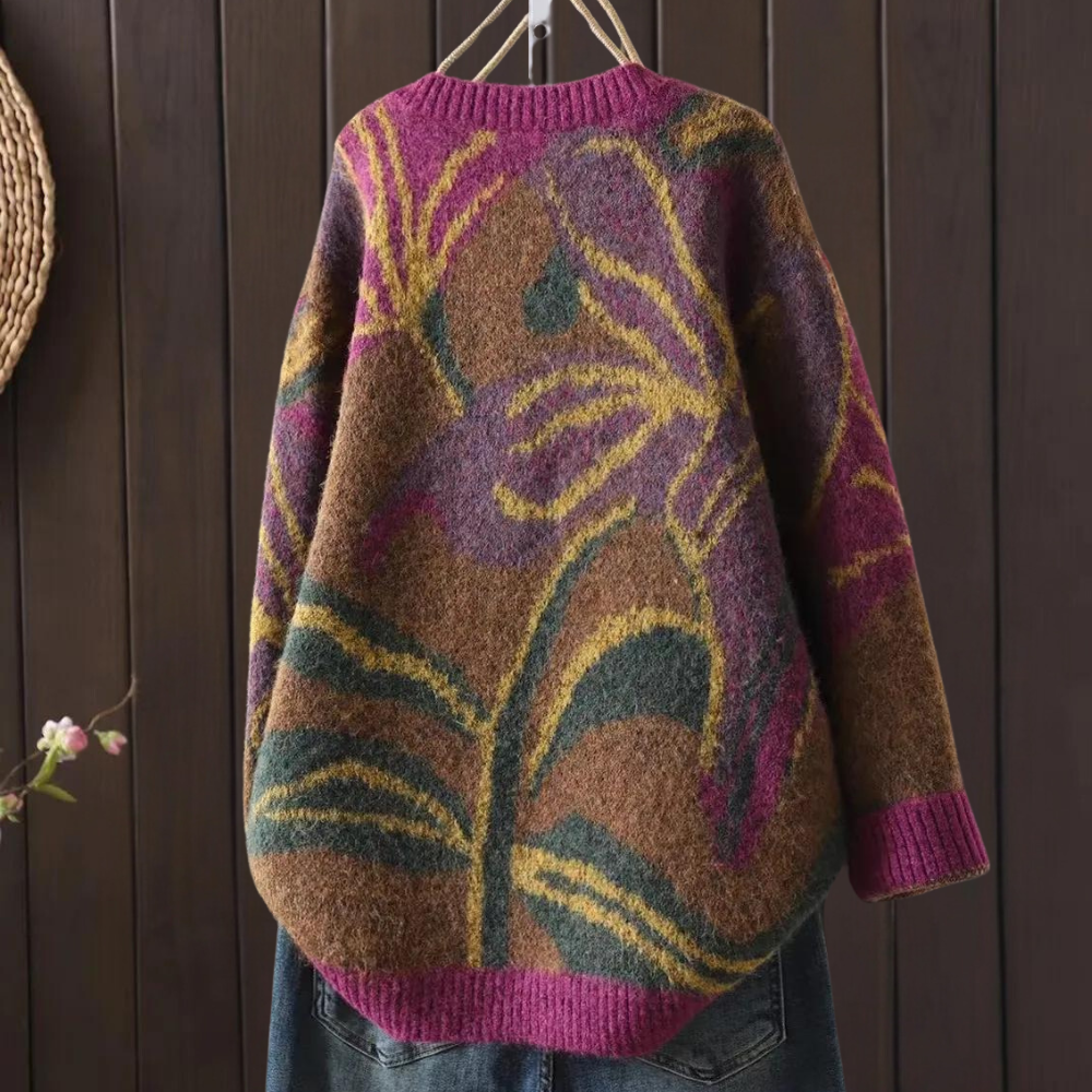 Gebreide trui met kleurrijk bloemenpatroon, hangend aan een houten muur. Perfect voor herfstmode, warme en stijlvolle dameskleding.