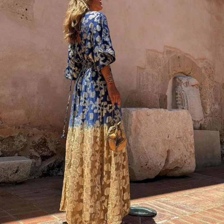 Stijlvolle damesjumpsuit met blauwe en gouden bloemenprint, lange mouwen, elegante uitstraling, perfect voor zomerse gelegenheden.