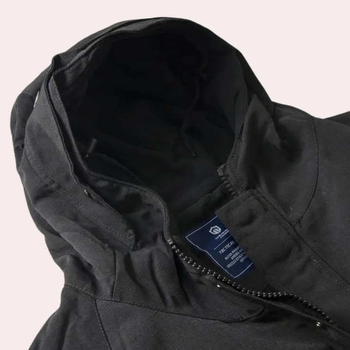 Zwarte technische jas met capuchon, ritssluiting en label, ideaal voor outdoor activiteiten. Waterafstotend en duurzaam materiaal.
