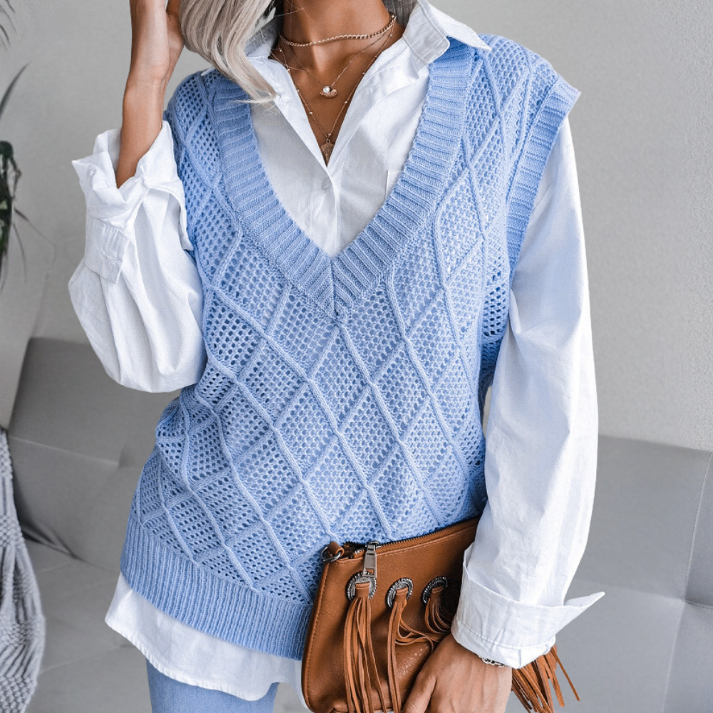 Vrouw in blauwe gebreide spencer over witte blouse, met bruine leren tas. Modieuze dameskleding, herfstoutfit, casual stijl.